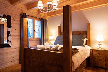 A cozy, wood-paneled chalet bedroom with a large wooden four-poster bed, warm lighting, and rustic decor.