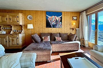 A cozy alpine-style living room with wood paneling, a brown sectional sofa, and a colorful highland cow painting on the wall.