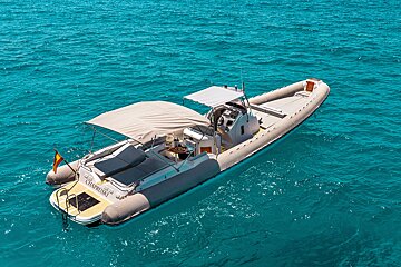 A luxury rigid inflatable boat with a beige canopy floats on clear, turquoise water.