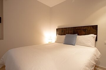 Cozy minimalist bedroom featuring a bed with white bedding, a rustic wood headboard, and a soft blue accent pillow.
