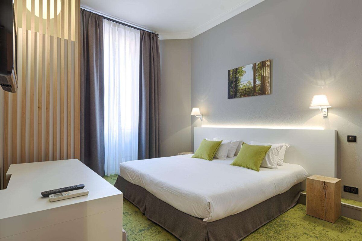 A hotel room with a white bed and green pillows