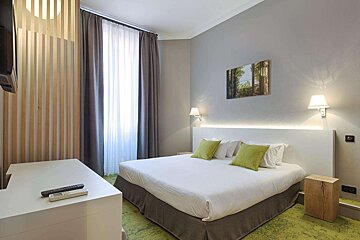 A hotel room with a white bed and green pillows