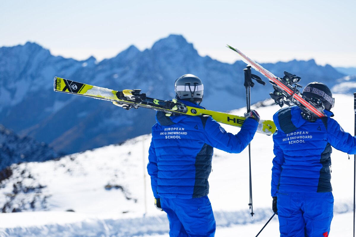 Two people wearing blue jackets that say european ski and snowboard school