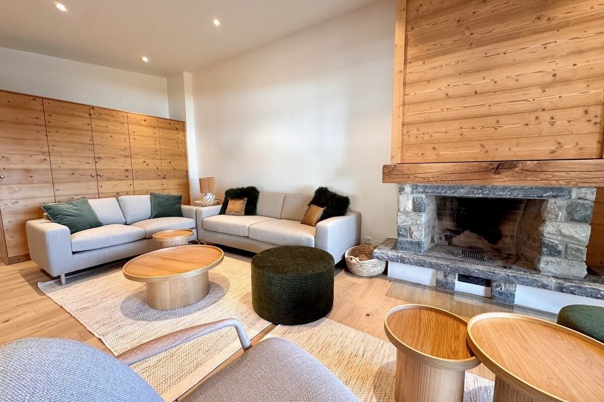 A modern living room with light sofas, wood paneling, wooden tables, and a stone fireplace, creating a cozy and natural ambiance.