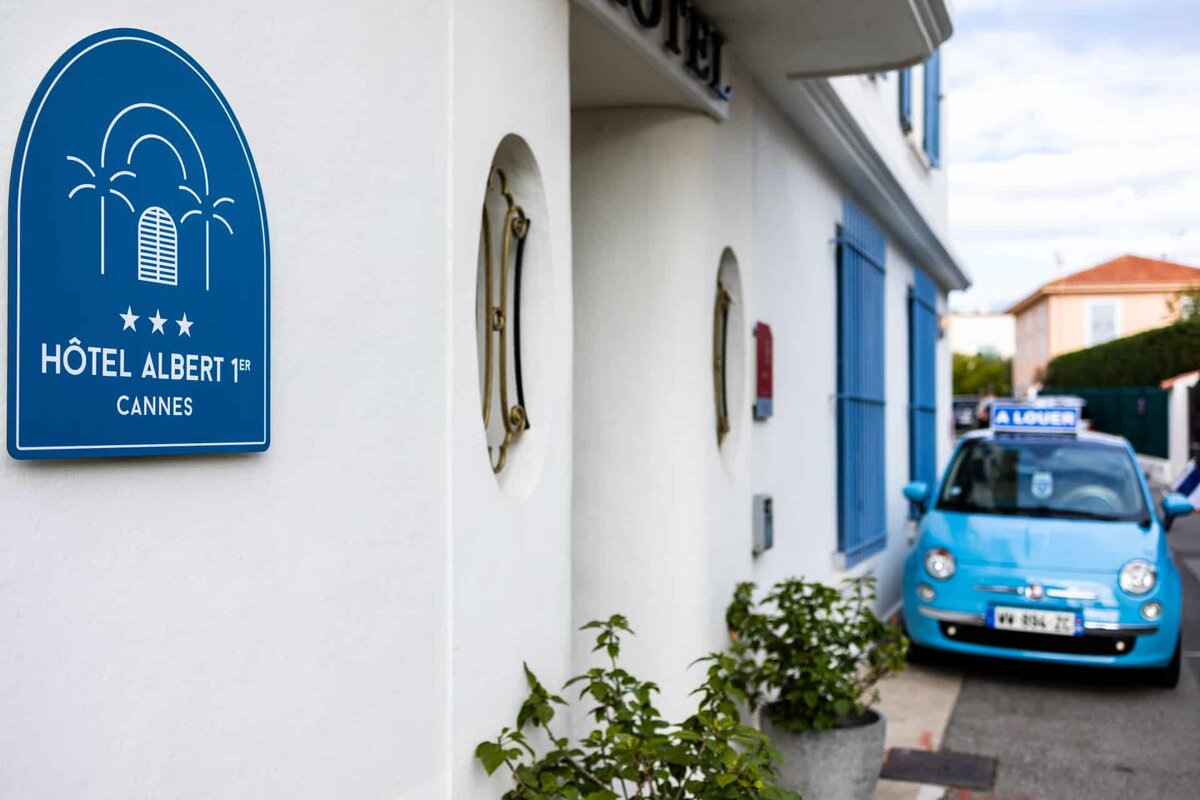 A blue car is parked in front of the hotel albert cannes