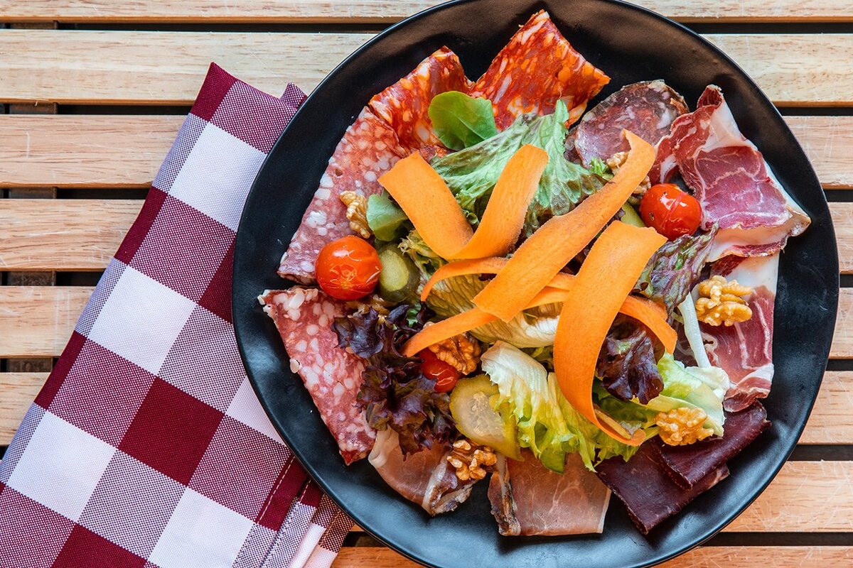 A black plate topped with meats and vegetables on a checkered napkin