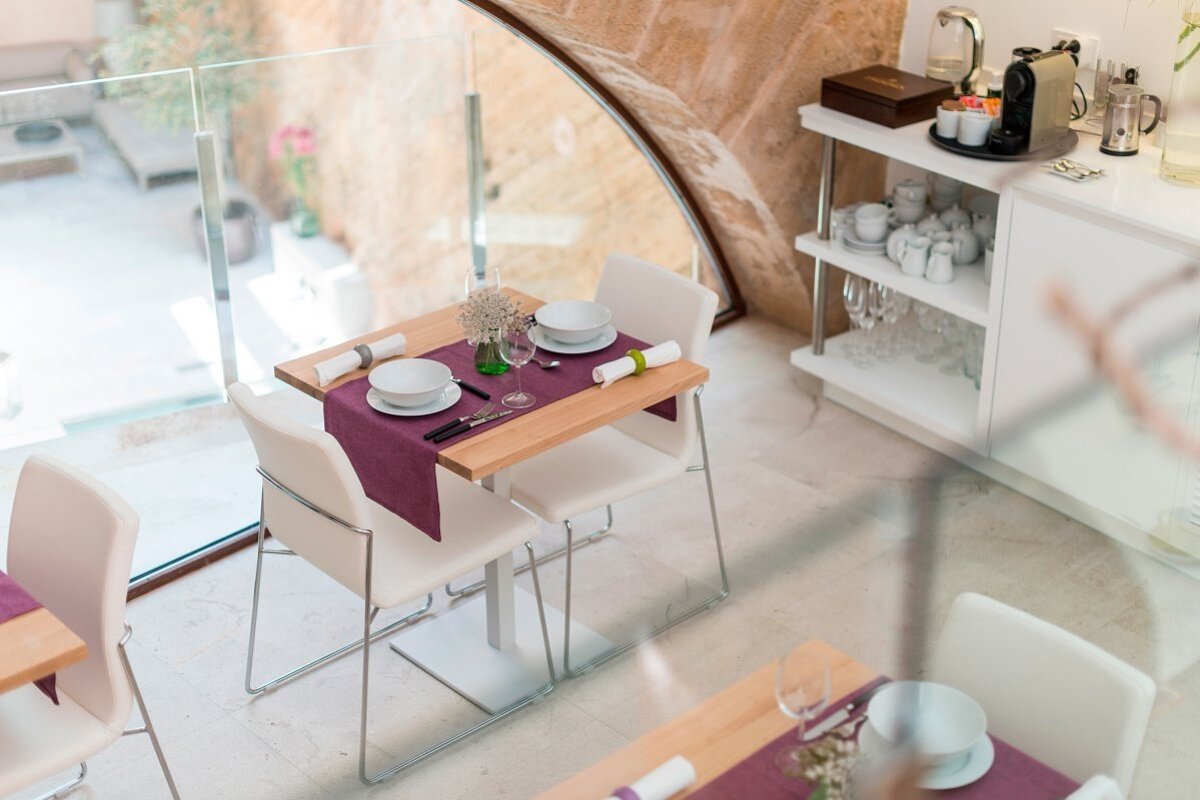 A bright, modern dining area with tables set with purple runners and white chairs. A glass railing offers views, alongside a coffee/tea station.
