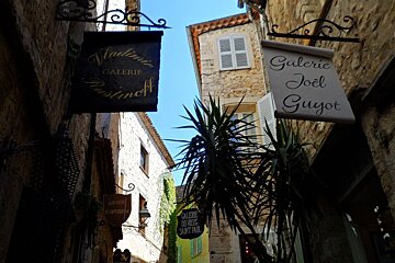 two signs hanging from stone walls in a shady street