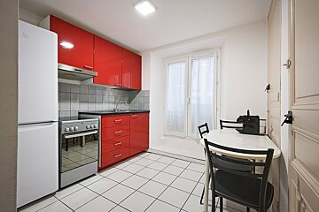 A kitchen with red cabinets and a white refrigerator that says indesit