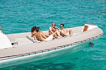 Four friends relaxing and sunbathing on a white motorboat in clear turquoise ocean water.