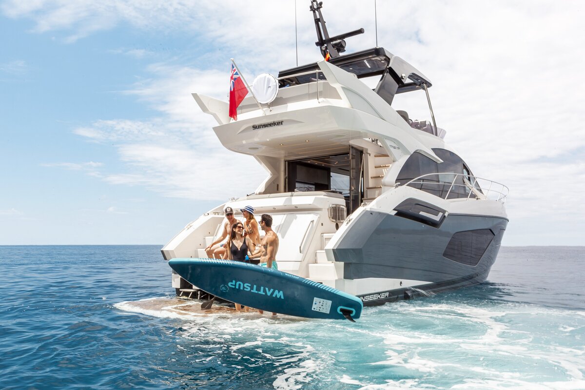 A group of people on a boat with a surfboard that says wattsup on it