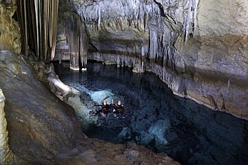 A group of people are swimming in a cave with icicles hanging from the ceiling
