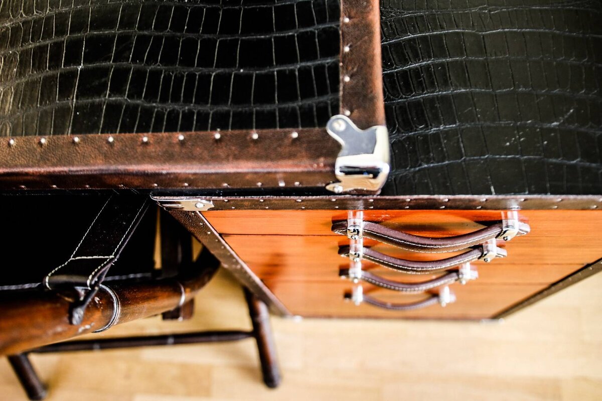 A trunk with leather handles sits on top of a desk