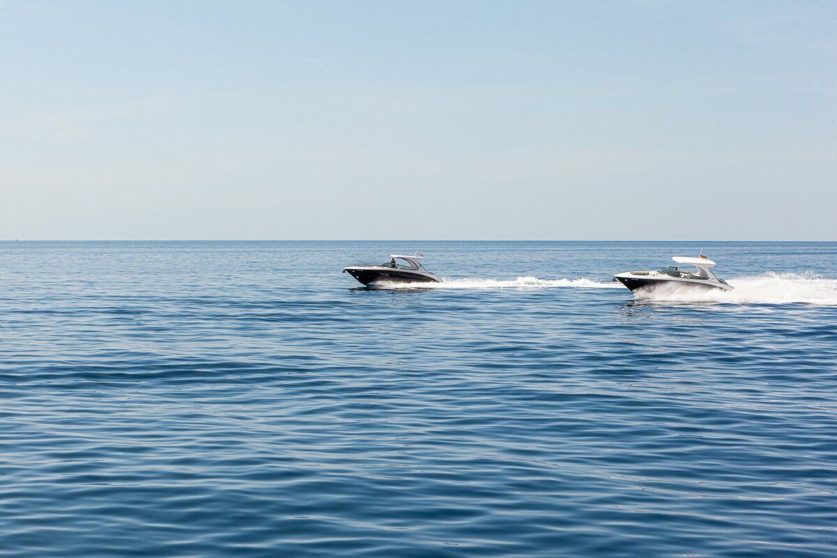Two motorboats speed across a vast, deep blue sea under a clear sky, leaving trails of white wake.
