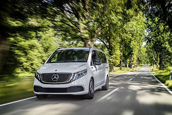 A white mercedes van is driving down a road