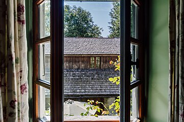 A window with a view of a house with shingles on the roof