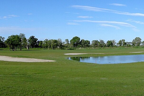 a golf green with water feature, sand bunker & blue skies