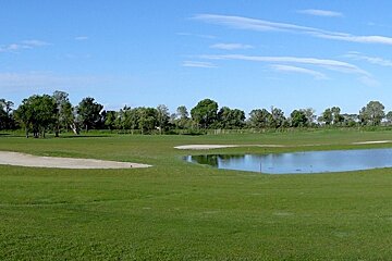 a golf green with water feature, sand bunker & blue skies
