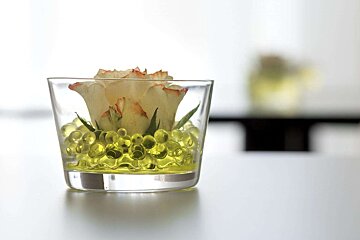 A glass filled with yellow beads and a flower in it