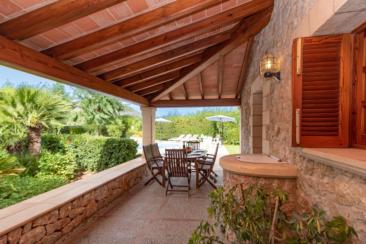A patio with a table and chairs under a wooden roof