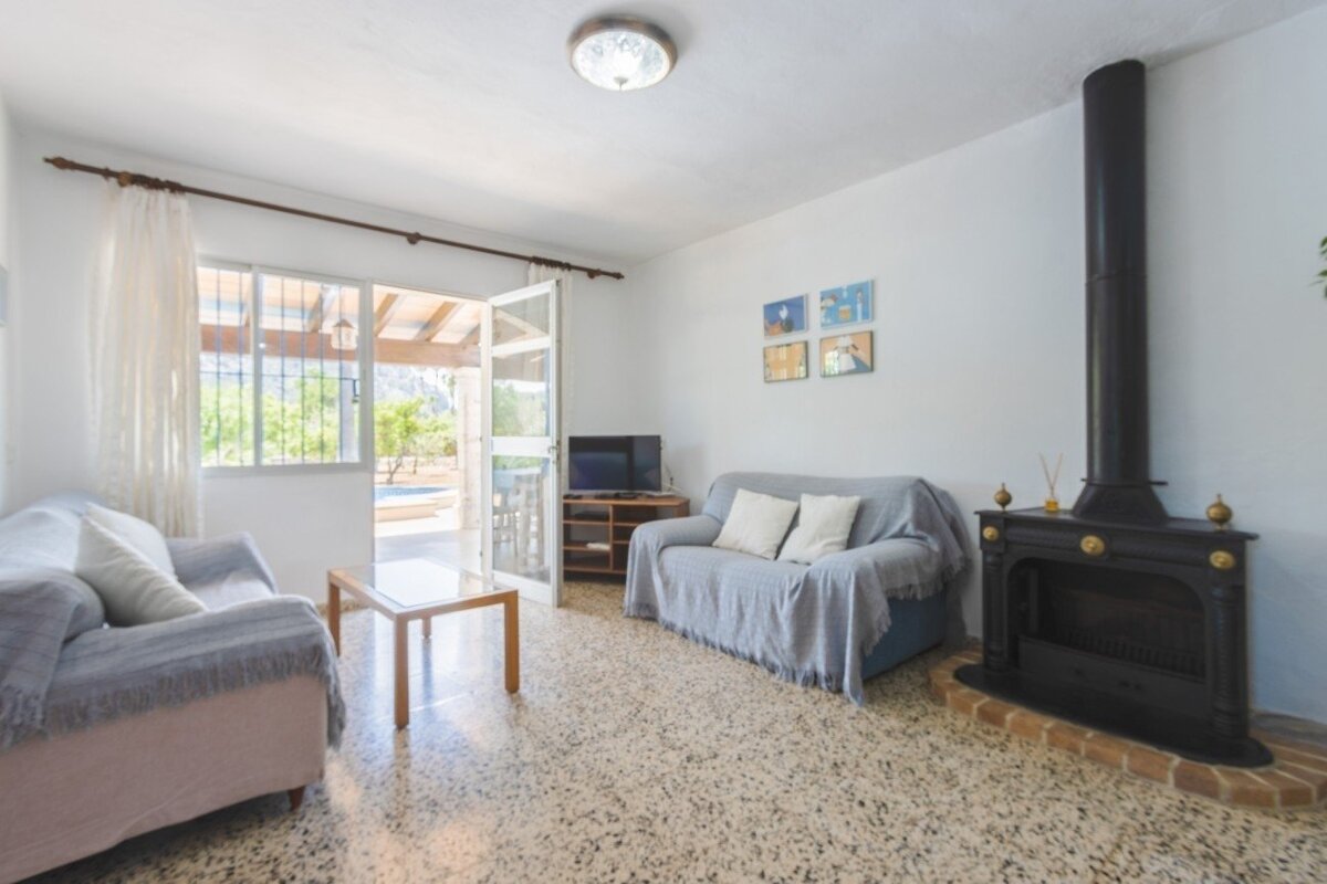 Bright living room with two sofas, a black fireplace, TV, and a glass door opening to a patio with a pool and mountain views.