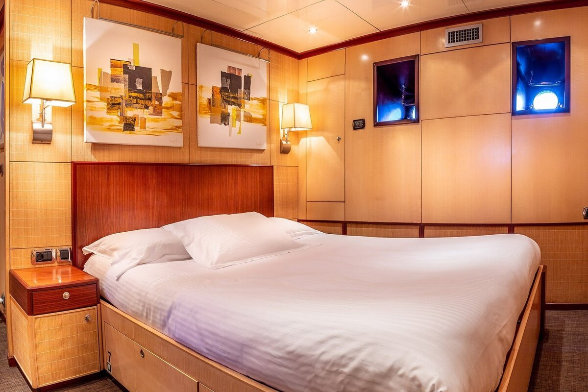 A luxurious bedroom with a large white bed, wooden paneled walls, abstract art, and ambient lighting, including blue-lit alcoves.