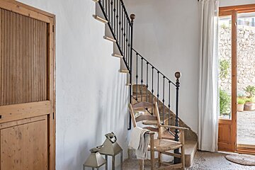 A wooden chair sits next to a staircase with a wrought iron railing