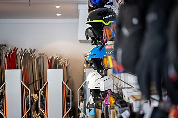 A ski shop interior displays rows of colorful helmets and goggles on the right, with racks of skis visible in the background on the left.