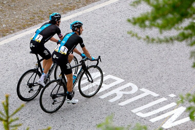 Two cyclists are riding down a road that has the word martin painted on it