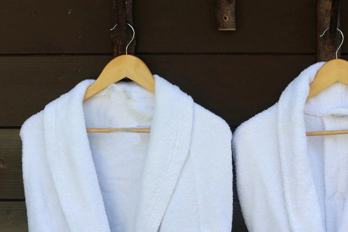 Two white bathrobes are hanging on wooden hangers