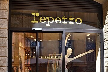 image of the outside of a shop with brick on the outside and gold writing and mannequin in the window