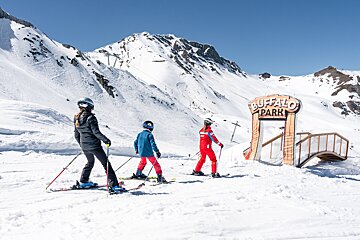 Three skiers on a sunny, snow-covered mountain, heading towards the