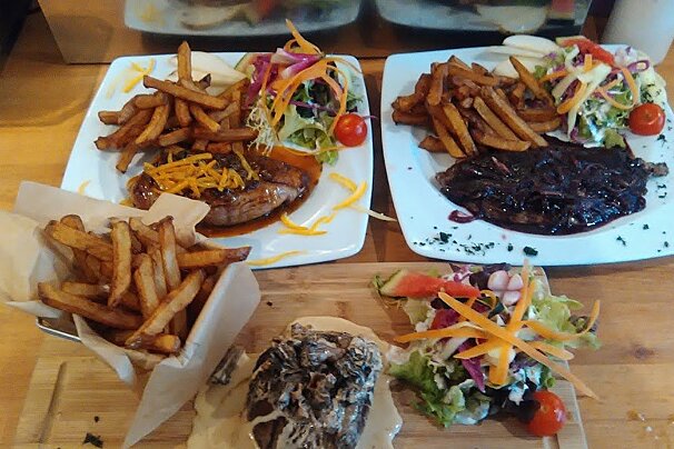 Two plates of food with french fries and salad on a wooden table
