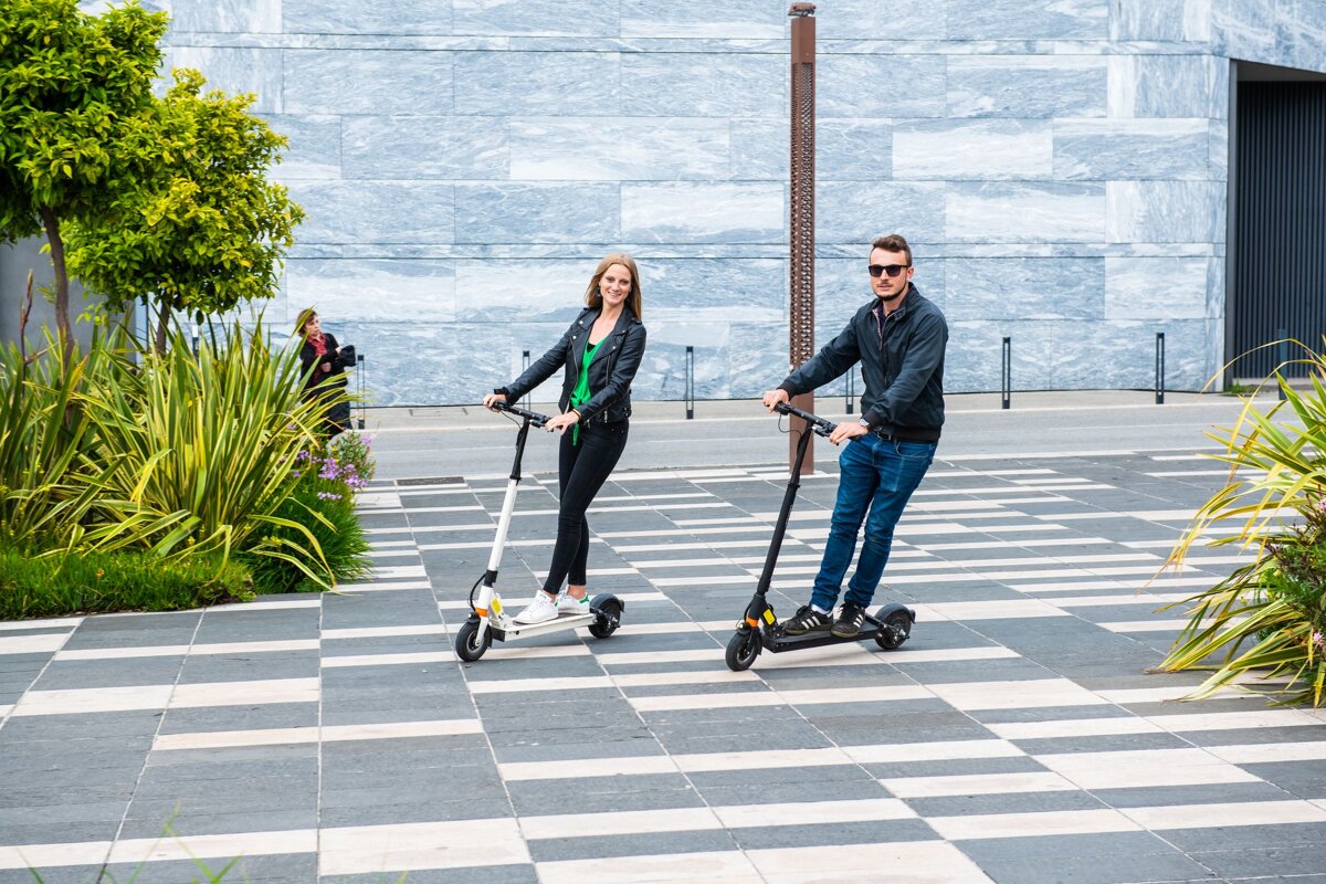 A man and a woman are riding scooters on a sidewalk