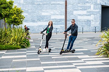 A man and a woman are riding scooters on a sidewalk