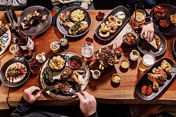 A table topped with plates of food and drinks including a bottle of barbecue sauce