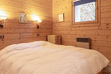 Cozy bedroom with light wood paneling, a large bed, window overlooking autumn trees, and warm wall lighting.