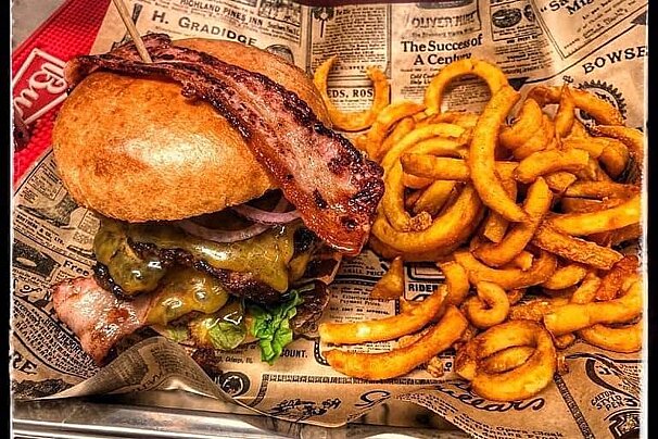 A hamburger with bacon and french fries on newspaper