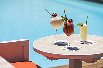 Three drinks on a table next to a pool