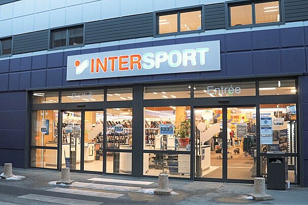 Exterior view of an Intersport store with a blue facade, large glass entrance doors, and a visible, illuminated interior.