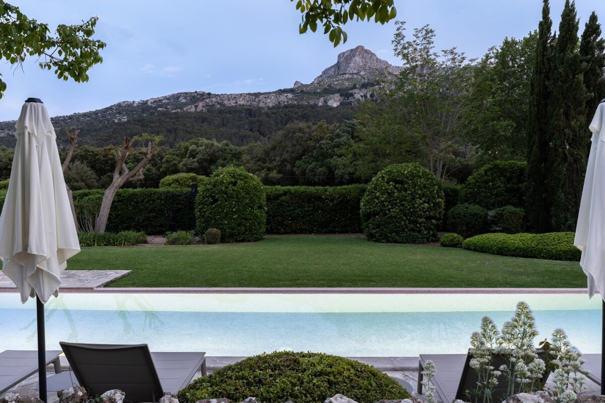 A swimming pool surrounded by chairs and umbrellas with a mountain in the background
