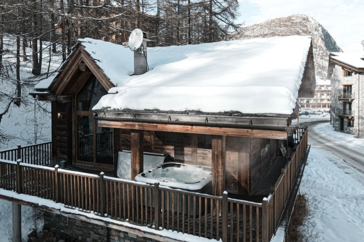 A snowy cabin with a hot tub on the deck