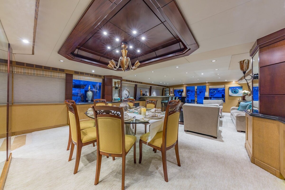 Elegant yacht interior featuring a dining area with yellow chairs, a grand chandelier, and a cozy lounge, all with blue window views.