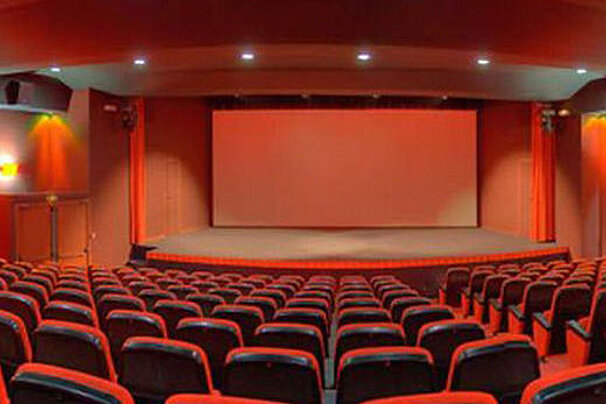 An empty movie theater with red seats and a large screen