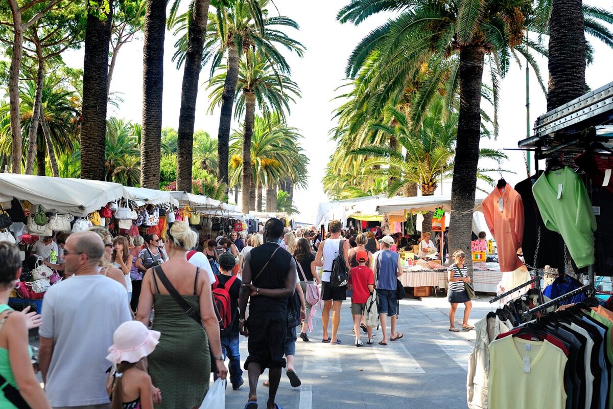 A crowd of people are shopping at a market with a sign that says ' t-shirts ' on it