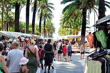 A crowd of people are shopping at a market with a sign that says ' t-shirts ' on it