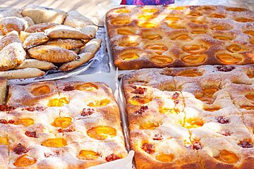 A vibrant display of baked goods: large, sugar-dusted fruit tarts with apricots and berries, next to a platter of smaller pastries.