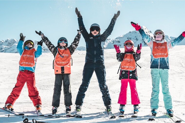 A group of children wearing ski vests that say supreme