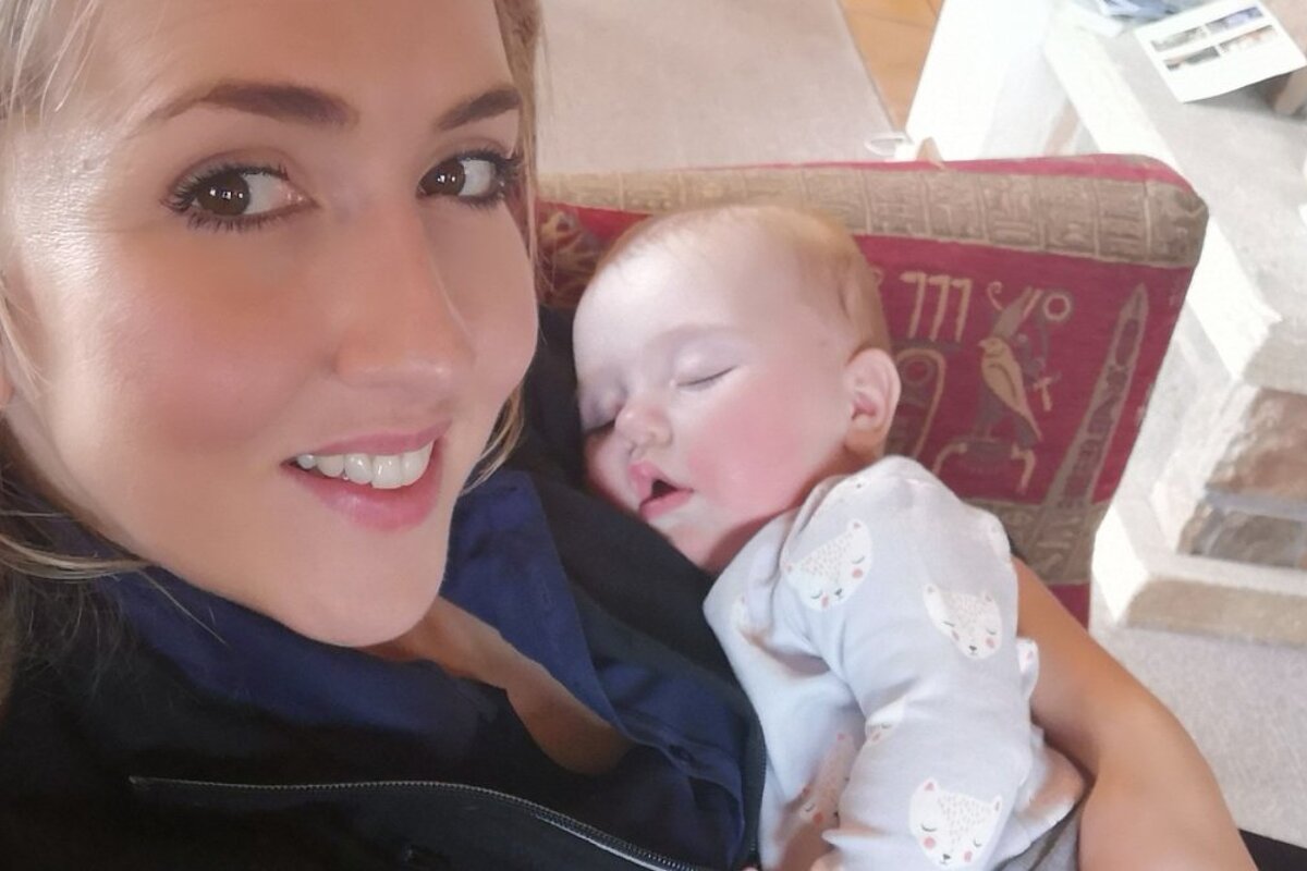 A woman holds a baby in front of a red pillow with the number 777 on it