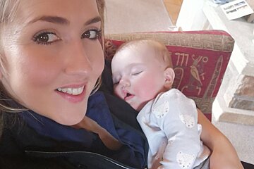 A woman holds a baby in front of a red pillow with the number 777 on it